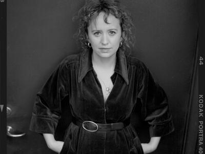 Sort-hvidt portræt af forfatteren Olga Ravn i mørk kjole med bælte, stående foran en mørk baggrund.