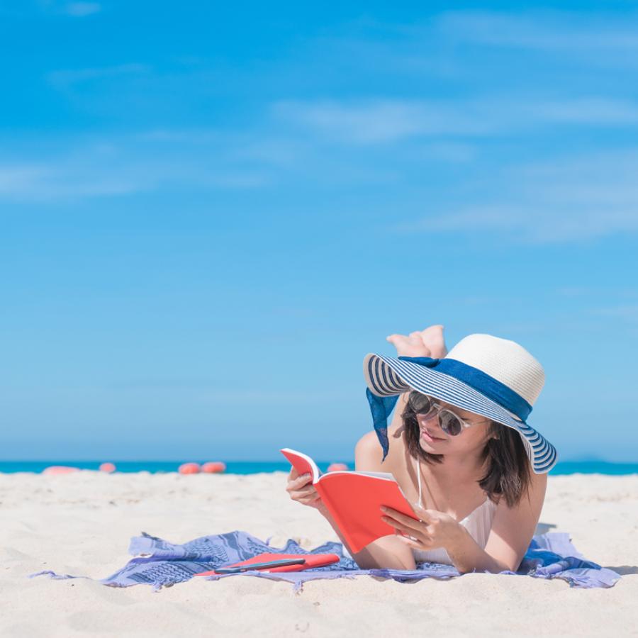 Foto: Kvinde på strand læser en bog